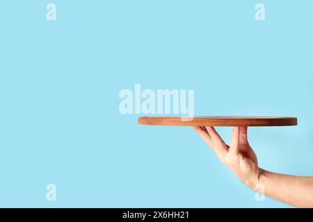 Man hand holding a brown round wooden plate on a blue background with copy space Stock Photo