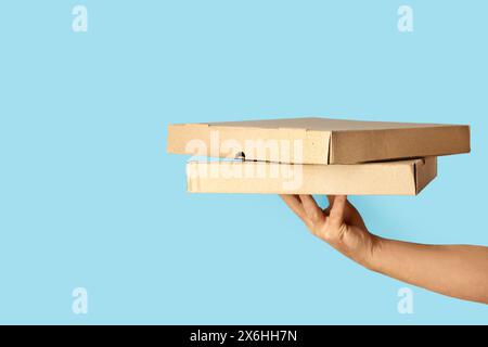 Man hand holding two brown cardboard pizza boxes on a blue background with copy space Stock Photo