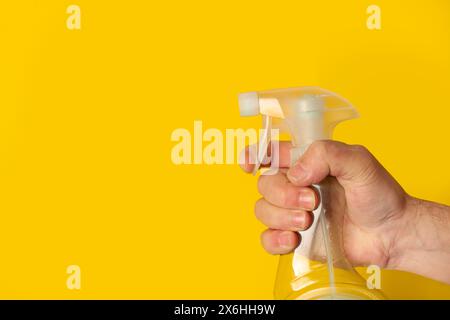 Man hand holding a sprayer bottle on a yellow background with copy space Stock Photo