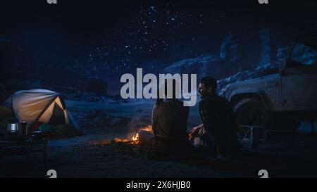 Happy Couple Tent Camping in the Canyon, Sitting by Campfire Watching Night Sky with Milky Way Full of Bright Stars. Two Travelers In Love On a Romantic Vacation Trip. Back View Shot Stock Photo