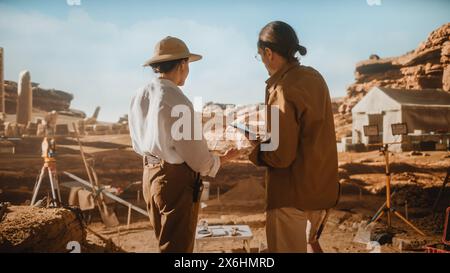 Archaeological Digging Site: Two Great Archeologists Work on Excavation Site, Use Map and Digital Tablet Computer to Inspect Newly Discovered Ancient Civilization Architectural Site, Planning Work Stock Photo