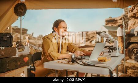 Archaeological Digging Site: Smart Male Archaeologist Doing Research, Using Laptop, Analysing Fossil Remains, Ancient Civilization Culture Artifacts. Team of Historians work on Excavation Site Stock Photo