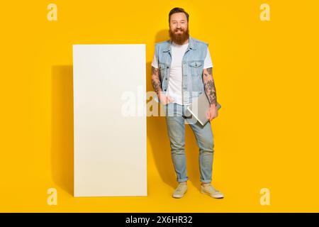 Photo of funny cute man wear jeans waistcoat holding modern device empty space isolated yellow color background Stock Photo