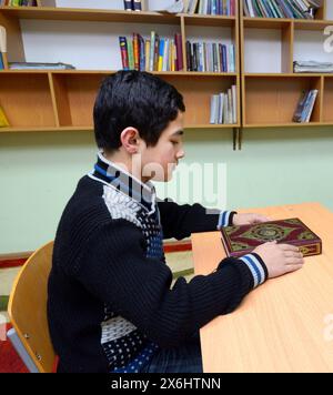 Classroom of the medrese. Muslim boy sitting at a school desk, Quran placed in front of him. October 21, 2018. Islamic culture centre, Kiev, Ukraine Stock Photo