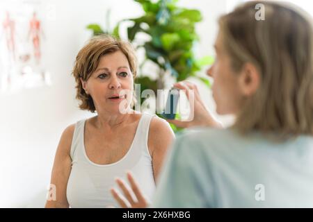 Elderly woman using asthma inhaler in clinic Stock Photo