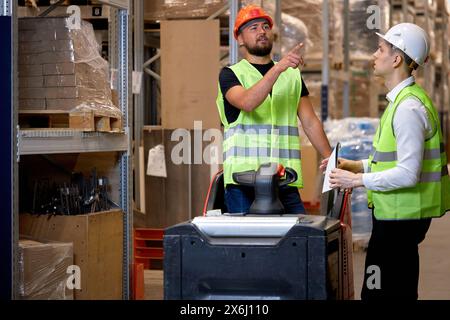 Young caucasian men workers doing stocktaking of products on shelves in warehouse together, using clipboard and forklift, having talk discussing, cont Stock Photo