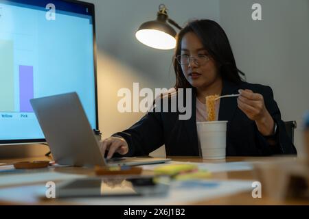 The woman ate instant noodles while working late at the office. Stock Photo