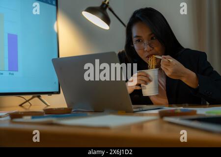 The woman ate instant noodles while working late at the office. Stock Photo