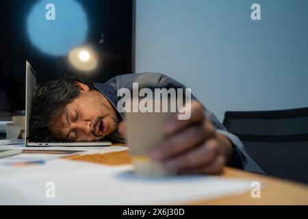 The man who worked hard fell asleep with a cup of coffee at the office. Stock Photo