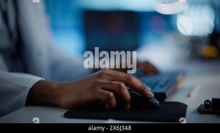 Modern Electronics Research, Development Facility: Engineer Working on Computer, Using Computer Mouse with His Hand. Scientist Design PCB, Silicon Microchips, Semiconductors. Close-up Focus on Hands Stock Photo