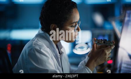 Modern Electronics Research and Development Facility: Beautiful Black Female Engineer Inspects Printed Circuit Board Motherboard. Scientist Designs Industrial PCB, Silicon Microchips, Semiconductors Stock Photo