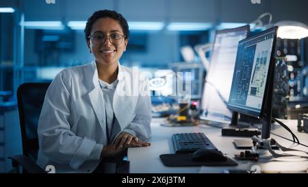 Beautiful Black Latin Woman Wearing Glasses Smiling Charmingly Looking at Camera. Young Intelligent Female Scientist Working in Laboratory. Technological Laboratory in Bokeh Blue as Background Stock Photo