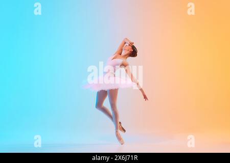 Profile view of artistic ballerina dancing, leaning backwards elegantly in neon light against blue-orange gradient background. Stock Photo