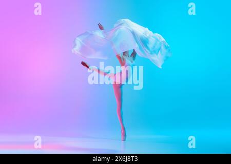 Elegant female dancer performing ballet move with white fabric in motion in neon light against vivid gradient background. Stock Photo