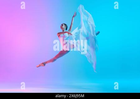 Ballet dancer performs jumping split in motion with flowing white cloth in neon light against vivid gradient background. Stock Photo