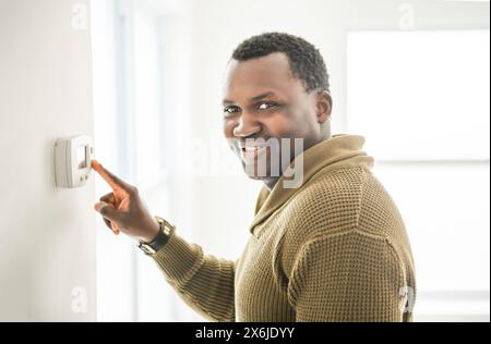 man choosing temperature on thermostat. Young focused guy pushing button home system. Stock Photo