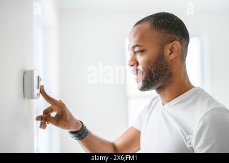 man choosing temperature on thermostat. Young focused guy pushing button home system. Stock Photo