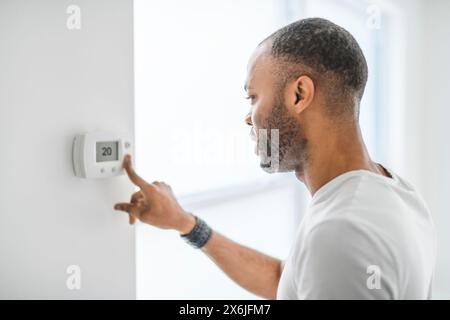 man choosing temperature on thermostat. Young focused guy pushing button home system. Stock Photo