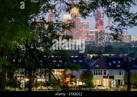 Seen through the branches of trees in Ruskin Park are the lit porches of terraced period homes and in the distance, the growing development at Nine Elms, on 14th May 2024, in London, England. Stock Photo