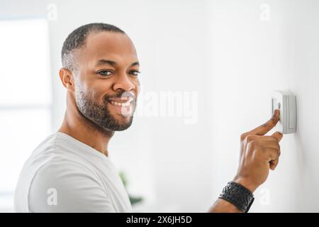 man choosing temperature on thermostat. Young focused guy pushing button home system. Stock Photo