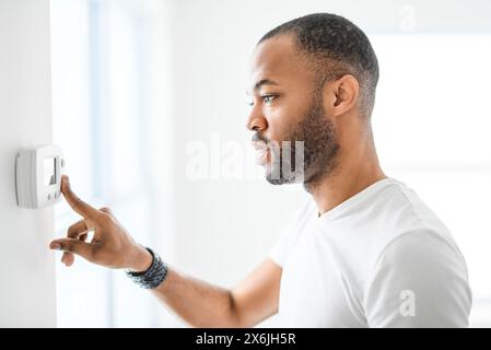 man choosing temperature on thermostat. Young focused guy pushing button home system. Stock Photo