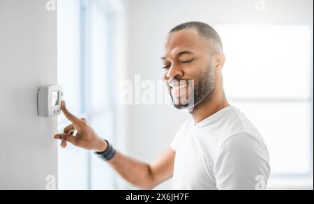 man choosing temperature on thermostat. Young focused guy pushing button home system. Stock Photo