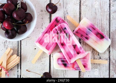 Healthy cherry yogurt popsicles. Top view table scene over a rustic white wood background. Stock Photo