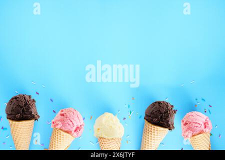 Ice cream bottom border over a blue background. Dark chocolate, pink strawberry and white vanilla flavors. Copy space. Stock Photo