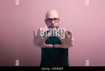 Portrait of bald, bearded man wearing prescription glasses showing his palm. Isolated on salmon colored background. Stock Photo