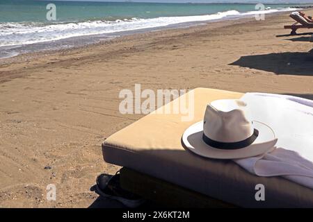 Sun Hat on Sun Lounger on Beach with Tourist Sunbathing in the Distance at The Chedi Hotel Beach Muscat Oman Stock Photo