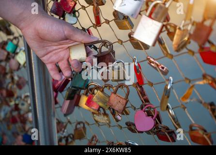 Salzburg, Austria, August 15, 2022. Close-up on the hand of a Caucasian young man holding one of the padlocks on the bridge of love. Conceptual image. Stock Photo