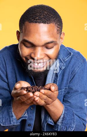 Coffee lover savoring the fresh aromatic black roasted scent, enthusiastic man holding a handful of coffee beans up to his nose and enjoying the c0old brew aroma, delicious flavor. Stock Photo