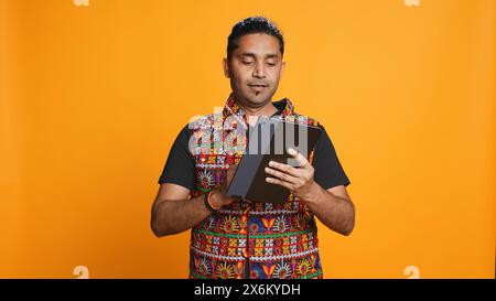 Man shakes head in disbelief after realizing lack of necessary funds while trying to shop online on tablet. Disappointed indian person gets credit card transaction rejected, studio backdrop, camera B Stock Photo