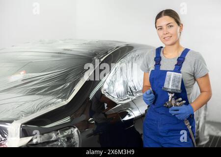 Young woman mechanic paints car with machine Stock Photo