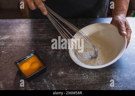 Baker's hands beating eggs with a hand mixer on a white plate, separating the yolks from the whites. Cooking in the traditional way Stock Photo