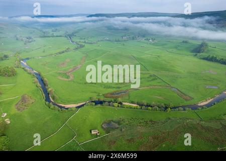 River Ure winding its way down Wensleydale near Hawes on an atmospheric late spring morning, with mist on the surrounding fells. North Yorkshire, UK. Stock Photo