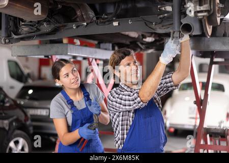 Male and female mechanics working on car on lift in auto repair shop Stock Photo