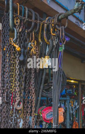 A selection of metal chains and hooks of various sizes hang from a metal pipe at a hardware store Stock Photo