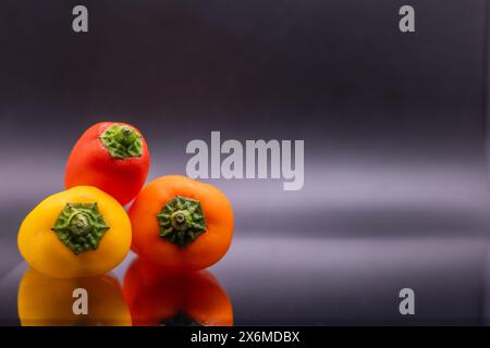 Red Yellow Orange mini bell peppers on black background isolated colorful display stacked left of center copy space right of frame texture shown Stock Photo
