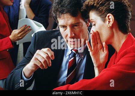 A male and female executive conferring buy whispering during a meeting Stock Photo