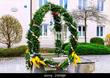 Easter fountain decorated with garlands of boxwood branches and colorful Easter eggs in front of the Old School in Forstinning in Upper Bavaria in Ger Stock Photo