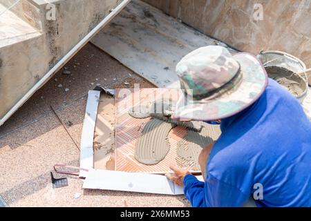 Worker tile mason spreading adhesive on tile for tiling wall. Stock Photo