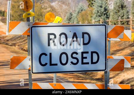 There is orange striped road closure sign near an ongoing construction project that preventing vehicles from driving Stock Photo