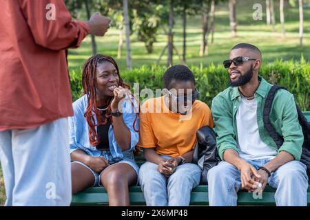 Carefree group african american diversity friends have fun outdoor sit on park bench laughs chating. Stock Photo