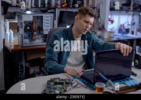 caucasian professional technician sit thinking how to repair fault laptop, sit behind table at workshop. Repairs and diagnostics breakdowns of laptop Stock Photo