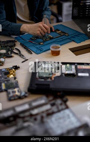 cropped male hands repairing parts in disassembled laptop using screwdriver and different tools on table in workshop. Hand technician repairing broken laptop notebook computer using tools Stock Photo