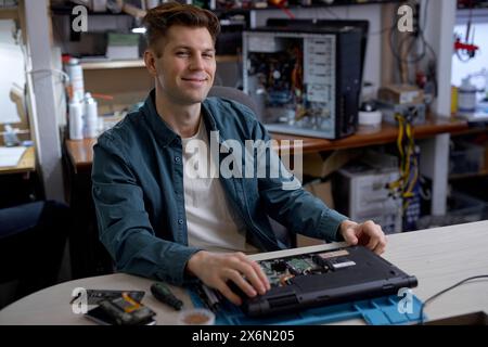 professional young repairman or technician repairs computers and laptop. portrait of service engineer in shirt repairing a laptop, happy guy looking at camera, posing, successful job Stock Photo