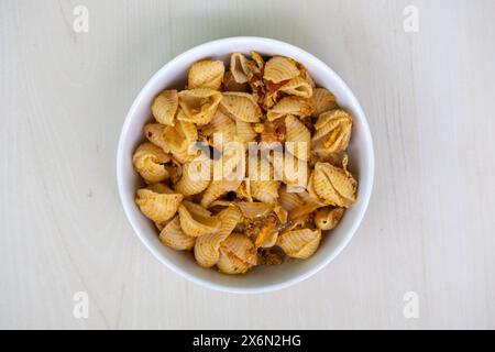 Delicious shell pasta in a white bowl on wooden background. Top view of tasty conchiglie rigate pasta. Stock Photo