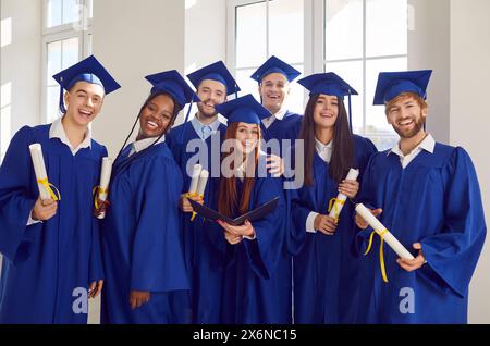 Diverse group of a young joyful graduate people looking at camera with diplomas in hands. Stock Photo