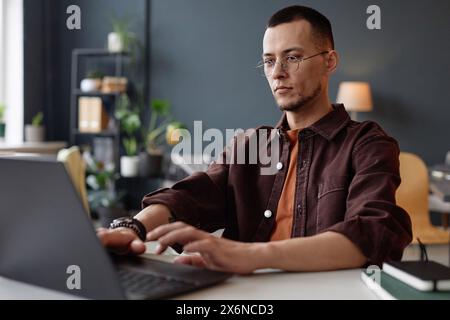 Portrait of young Asian man wearing glasses and using laptop in office with serious face expression Stock Photo
